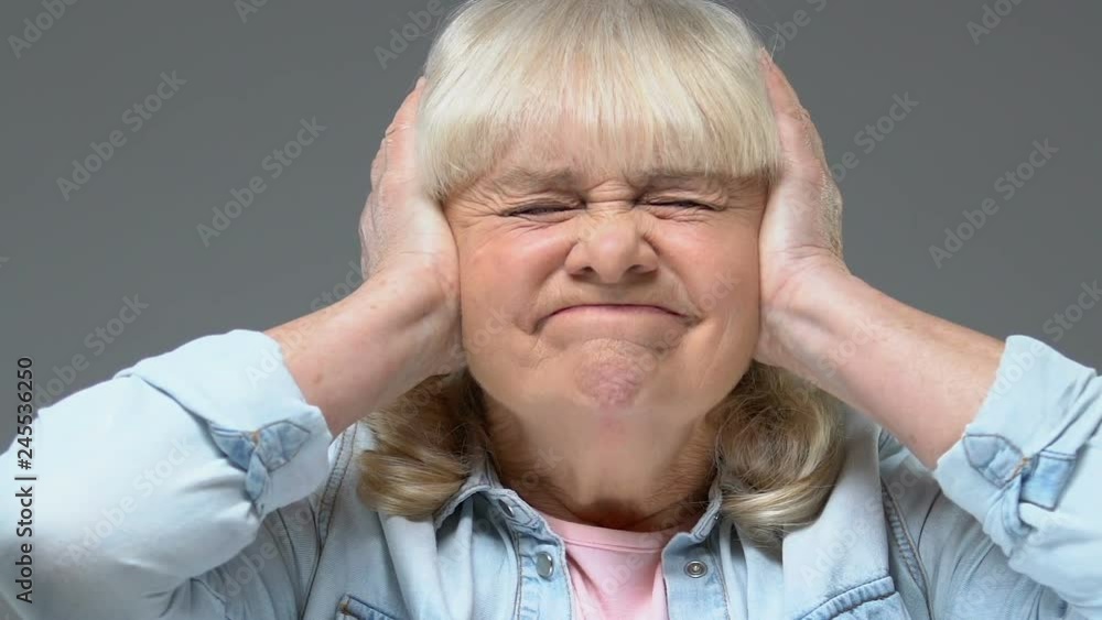 Annoyed grandmother covering ears by hands, loud sound stress, feeling headache