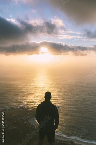 Young man standing on the edge at the top of Lion's head mountain in Cape Town with a beautiful sunset view © Dmitrii