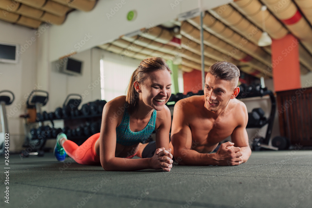 Obraz premium Young fit happy couple doing planking exercise in the gym