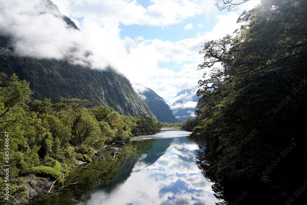 River surrounded by trees and mountains, with the reflections of clouds, Milford Track, New Zealand South Island 