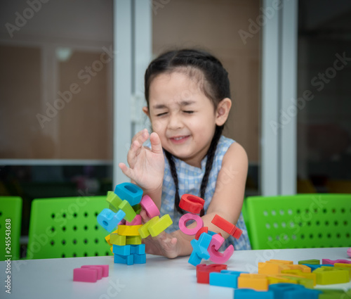 Cute kids female playing with toy designer on the floor at home. Child girl exciting while playing with alphabet colorful blocks. Kindergarten educational games for determination, intention concept