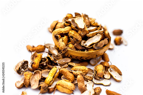 Close up of brown colored hamper having groundnuts or peanuts or moongaphalee or Arachis hypogaea or goober or monkey nut some in shells and some opened isolated on white.