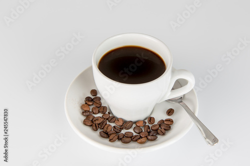 White Cup of black coffee on a white background, with some beans on the saucer