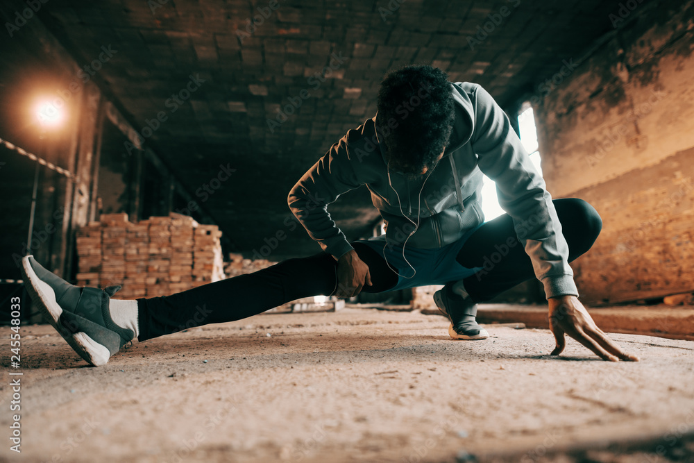 Close up of african american sporty man in sportswear and with earphones stretching leg after running. Healthy lifestyle concept. Close up of african american sporty man in sportswear and with earphones stretching leg after running. Healthy lifestyle concept.
