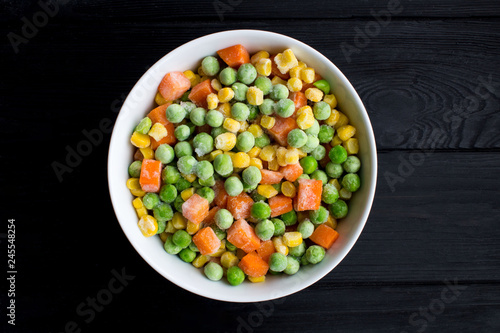 Frozen vegetables in the white bowl on the black wooden background.Top view.Copy space.Healthy food ingredients.