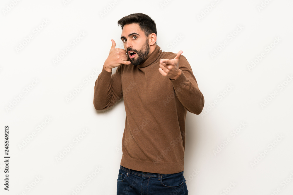 Handsome man over white wall making phone gesture and doubting Handsome man over white wall making phone gesture and doubting