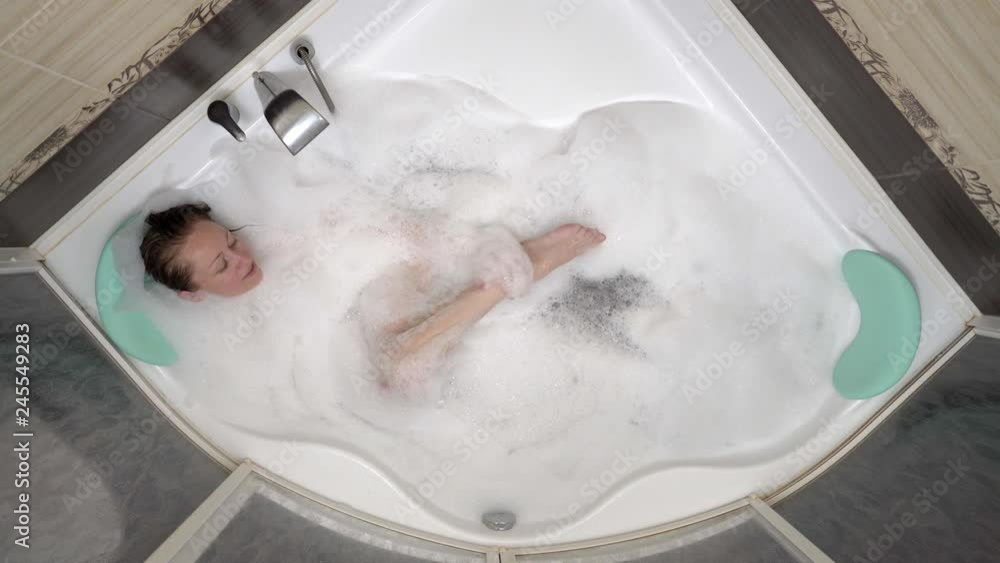 Beautiful young woman resting in bath with foam raises legs. Top view.
Beautiful young woman resting in bath with foam raises legs. Top view.