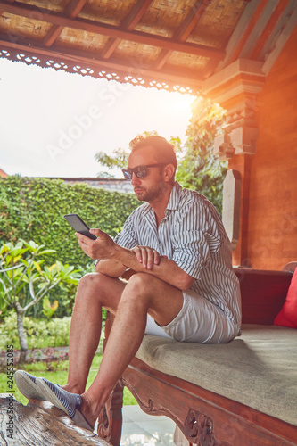 Man using smart phone on a terrace sofa in summertime. photo