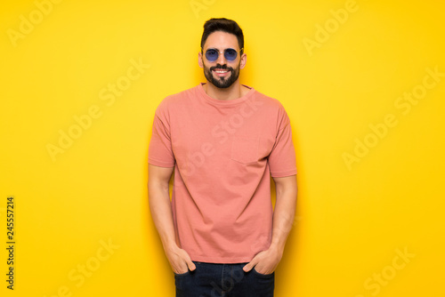 Handsome man over yellow wall with glasses and happy