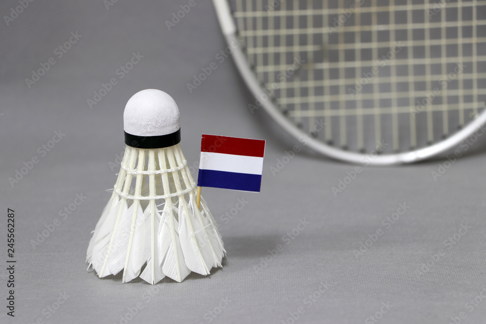 Mini Netherlands flag stick on the white shuttlecock on the grey background and out focus badminton racket.
