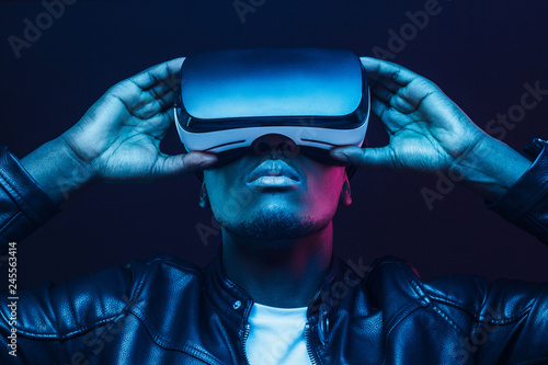 Portrait of African guy isolated on black background wearing headset of virtual reality photo