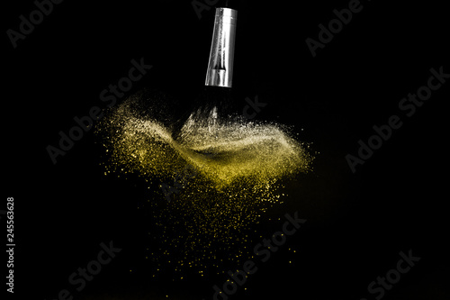 Cosmetic brush with golden cosmetic powder spreading for makeup artist and graphic design in black background