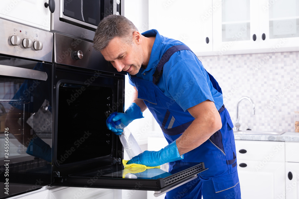 Obraz premium Male Janitor Cleaning Oven In Kitchen