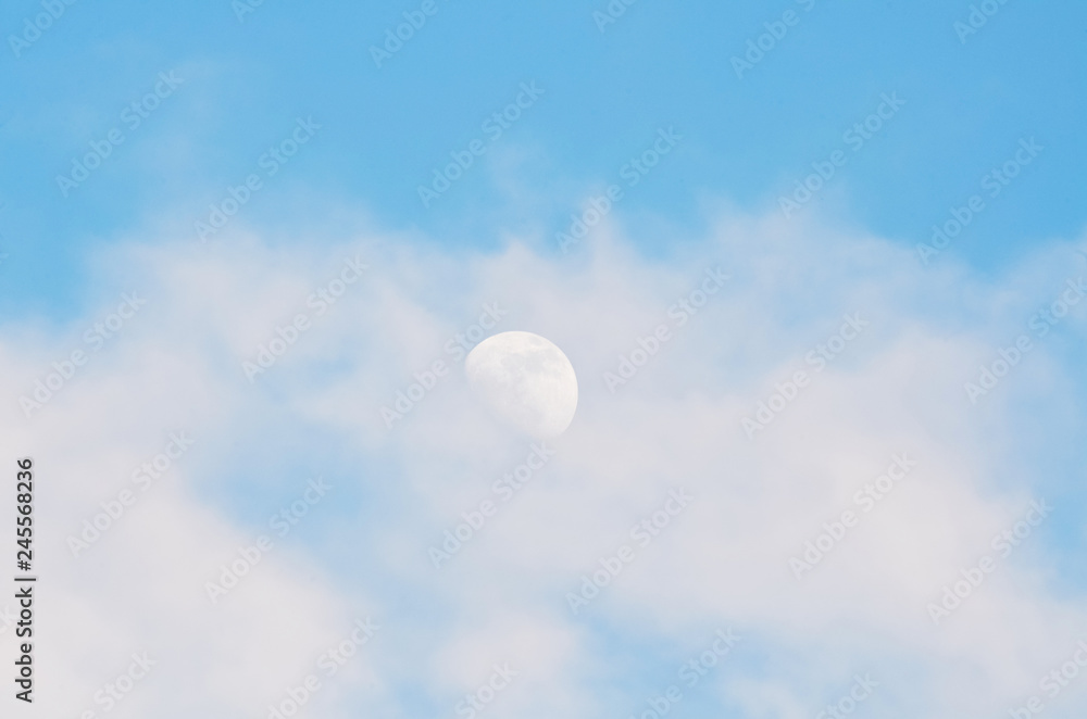 Half bright moon on blue sky background with clouds on day time Half bright moon on blue sky background with clouds on day time