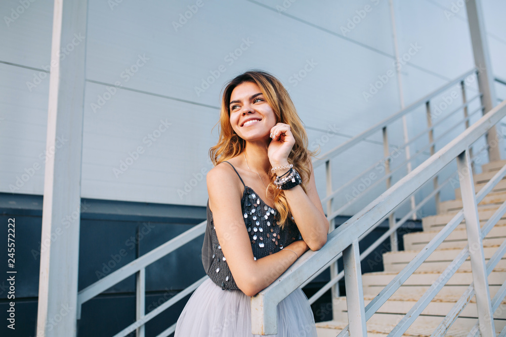 Portrait of beautiful model in grey shirt  leaning on handrail on stairs. She is smiling to side