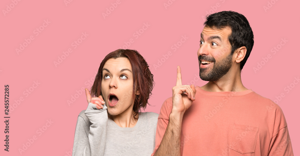 Couple in valentine day thinking an idea pointing the finger up over isolated pink background Couple in valentine day thinking an idea pointing the finger up over isolated pink background