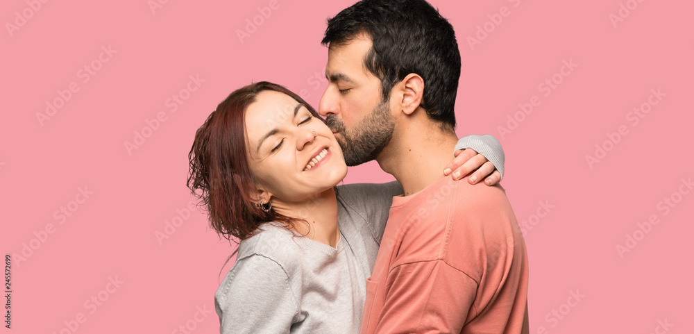 Couple in valentine day kissing over isolated pink background Couple in valentine day kissing over isolated pink background