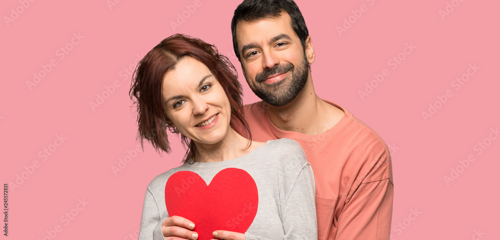 Couple in valentine day holding a heart symbol over isolated pink background Couple in valentine day holding a heart symbol over isolated pink background