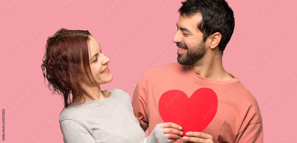Couple in valentine day holding a heart symbol over isolated pink background