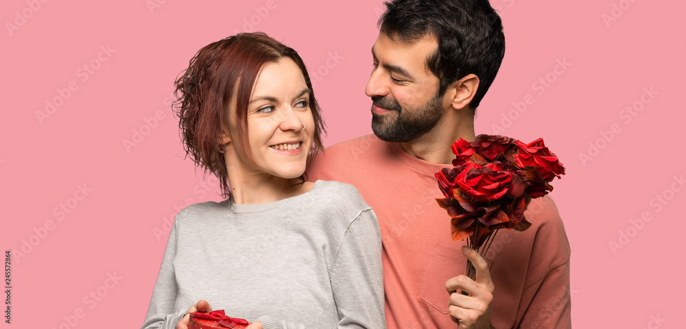 Couple in valentine day with flowers and gifts over isolated pink background