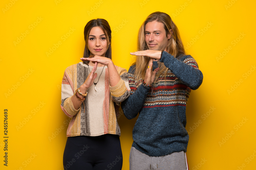 Hippie couple over yellow background making stop gesture with her hand to stop an act Hippie couple over yellow background making stop gesture with her hand to stop an act