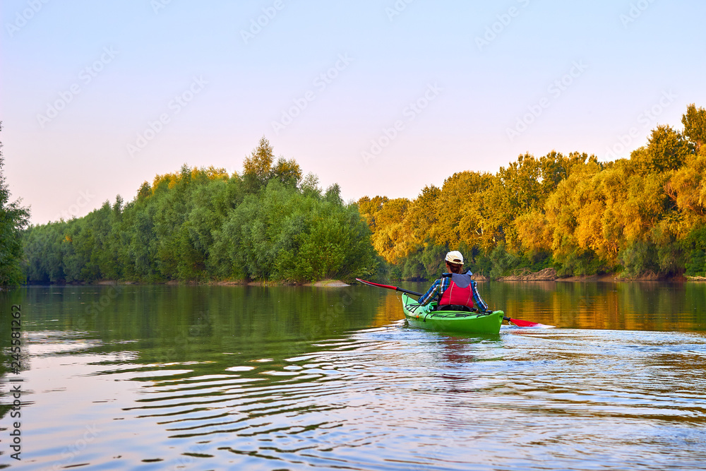 Woman paddle green kayak. Kayaking near overgrown shore of green thick thickets, wild grapes and driftwood on the banks of river at summer. Concept for adventure, travel, action, lifestyle. Woman paddle green kayak. Kayaking near overgrown shore of green thick thickets, wild grapes and driftwood on the banks of river at summer. Concept for adventure, travel, action, lifestyle.