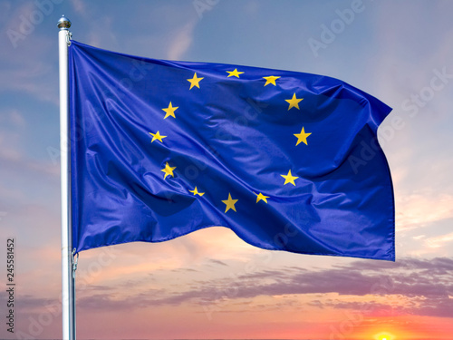 Flag of the European Union waving in the wind on flagpole against background of the sunrise, close-up