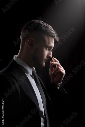 Elegant young fashion man in tuxedo .Sniffs cigar.Taste cigar. On black background