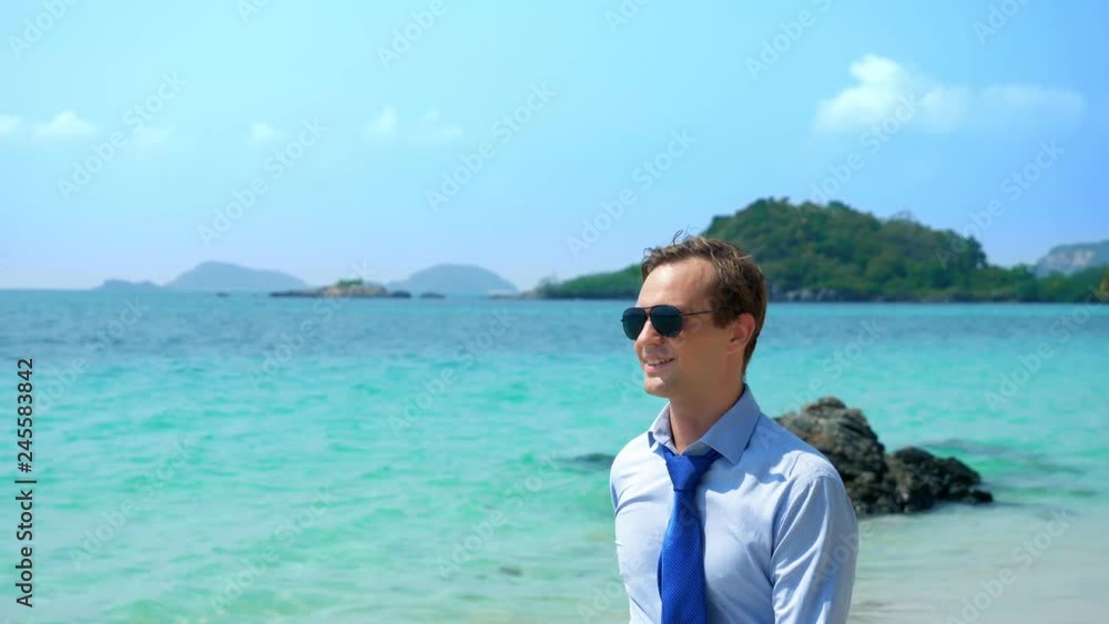 businessman in a shirt and tie, in sunglasses goes on a white sandy beach. freelancing concept, vacation businessman in a shirt and tie, in sunglasses goes on a white sandy beach. freelancing concept, vacation