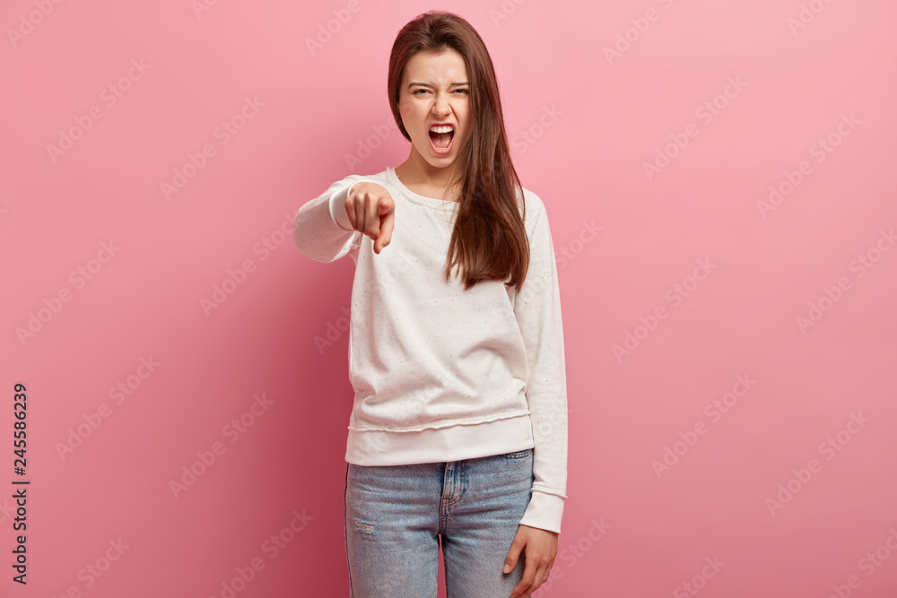 Strict dissatisfied woman points angrily directly at camera, exclaims with annoyance, frowns face in discontent, wears casual clothes, blames you, isolated over pink background, looks outraged Strict dissatisfied woman points angrily directly at camera, exclaims with annoyance, frowns face in discontent, wears casual clothes, blames you, isolated over pink background, looks outraged