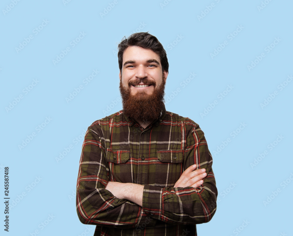 Photo of happy fashionable handsome bearded man in brown shirt crossing hands, smiling and looking at camera Photo of happy fashionable handsome bearded man in brown shirt crossing hands, smiling and looking at camera