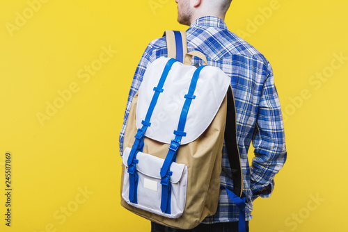 Handsome guy  in blue checkerd shirt with colorful  backpack on yellow background photo