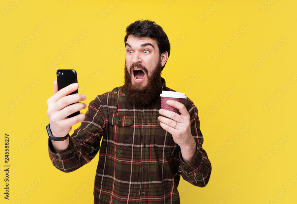 Photo of handsome excited bearded man drinking coffee and using his mobile Photo of handsome excited bearded man drinking coffee and using his mobile