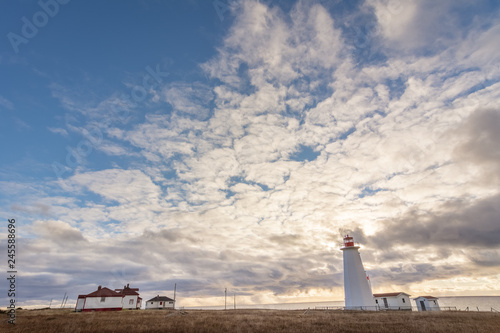 Lighthouse in Newfoundland, Canada with golden grasses in foreground, and stormy sunset  and blue sky in background