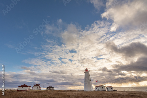Lighthouse in Newfoundland, Canada with golden grasses in foreground, and stormy sunset  and blue sky in background