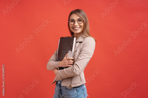 Young smiling student or intern in eyeglasses standing with a folder on red background. photo