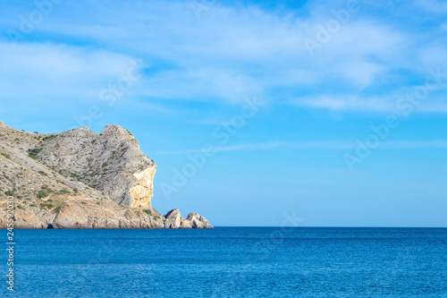 Beautiful sea landscape. Alchak mountain against the horizon and blue sky with light clouds, Sudak, Crimea.