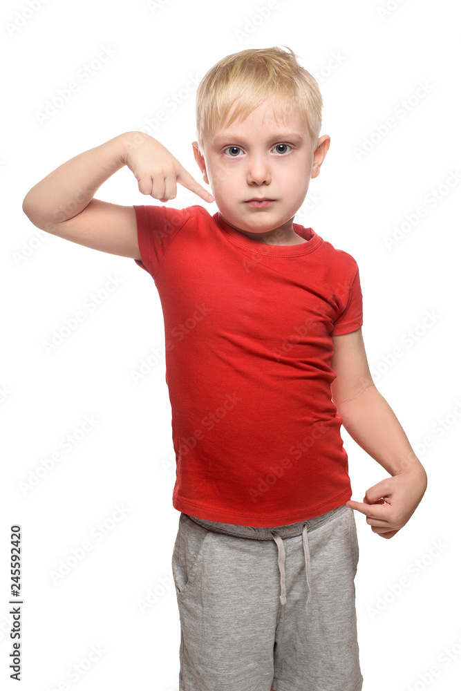 Blonde boy in a red shirt stands and shows index finger at yourself. Isolate on white background. Blonde boy in a red shirt stands and shows index finger at yourself. Isolate on white background.