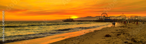 Scenic landscape of iconic Santa Monica Pier at orange sunset sky from the beach on Paficif Ocean. Santa Monica Historic Landmark, California, USA. Wide banner panorama. photo