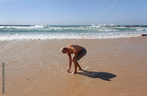 Resting man picks up a pebble from the sand photo