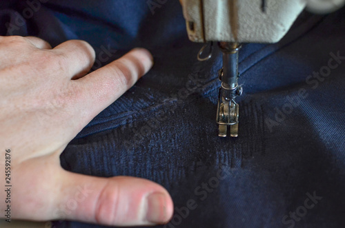 Male hand holding the fabric when sewing pants on a sewing machine. Stitching, stitch a hole in dark blue jeans or knit sweatpants with a sewing machine. Part of the sewing machine and denim closeup.