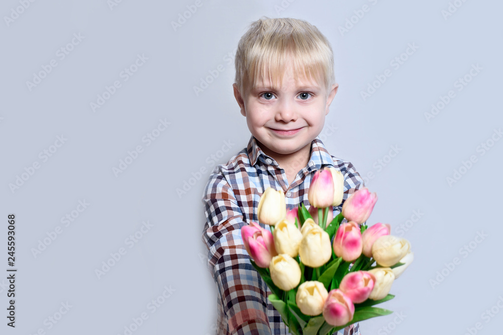 Small smiling blond boy holding a bouquet of tulips. Portrait on light background. Small smiling blond boy holding a bouquet of tulips. Portrait on light background.