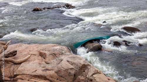 Capsized green canoe wedged between rocks and whitewater rapids in the James River Richmond, Virginia.