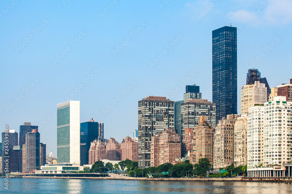 Fototapeta premium View of Midtown Manhattan skyline and the United Nations headquarters, viewed from Roosevelt Island over the East River during sunny summer day