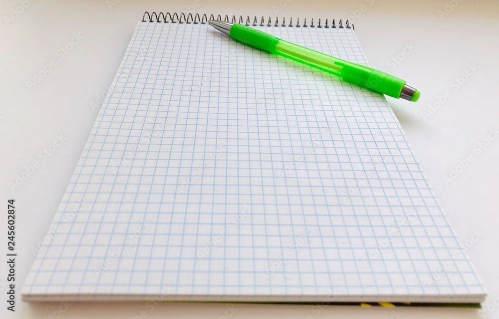 Checkered Notepad and a pencil on a white background. Things for study and work. Top view of a pad and pencil Checkered Notepad and a pencil on a white background. Things for study and work. Top view of a pad and pencil