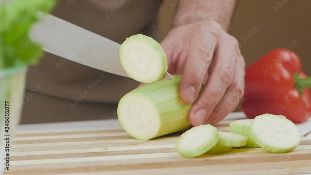 A man on a cutting board slices zucchini with a kitchen knife A man on a cutting board slices zucchini with a kitchen knife