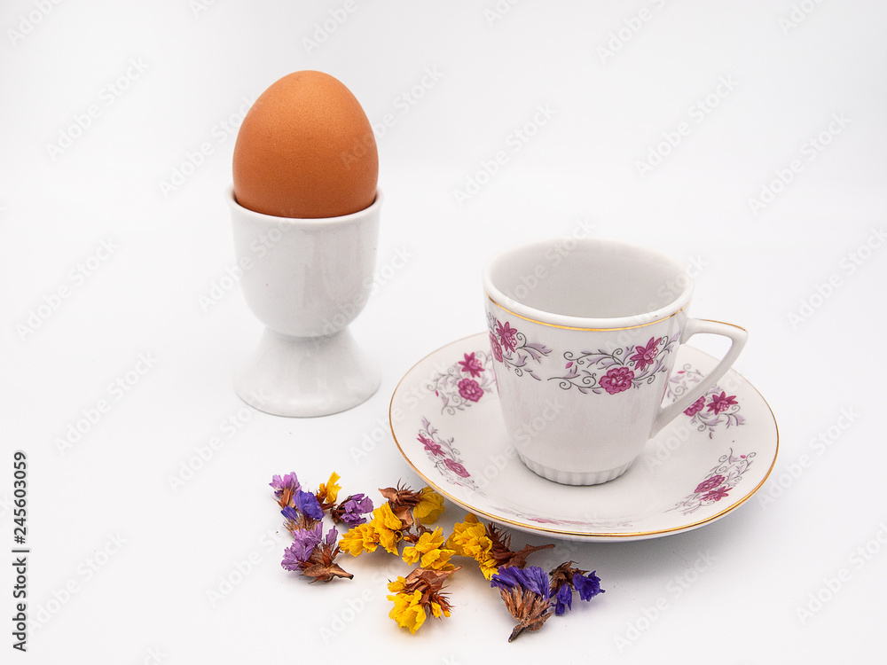 Beautifully designed espresso coffee cup with a hard cooked chicken egg in a porcelain egg holder with some dried limonium flowers isolated on a white background Beautifully designed espresso coffee cup with a hard cooked chicken egg in a porcelain egg holder with some dried limonium flowers isolated on a white background