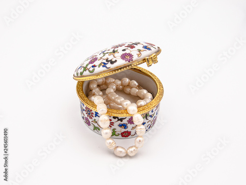 Beautifully ornamented porcelain jewelry box with a floral motive and a vintage flair with a sea pearls necklace showing from the inside isolated on a white background
