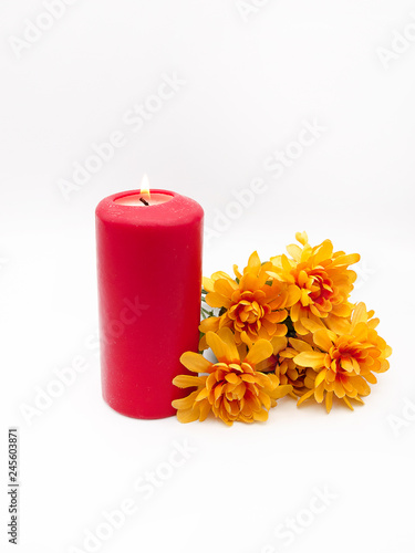 Lit red wax home interior candle with a bunch of synthetic chrysanthemum flowers isolated on a white background 