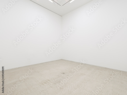 A view of a white painted interior of an empty room or an art gallery with a fluorescent lighting and concrete floors